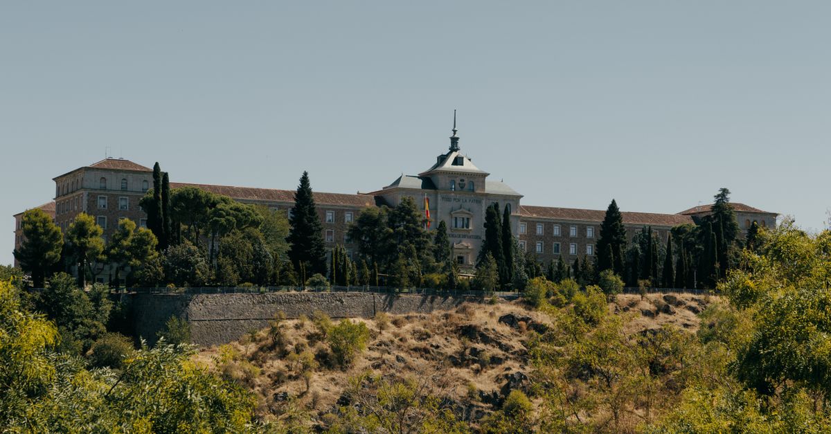 Historic Spanish Military Academy building in Toledo surrounded by trees under clear skies.